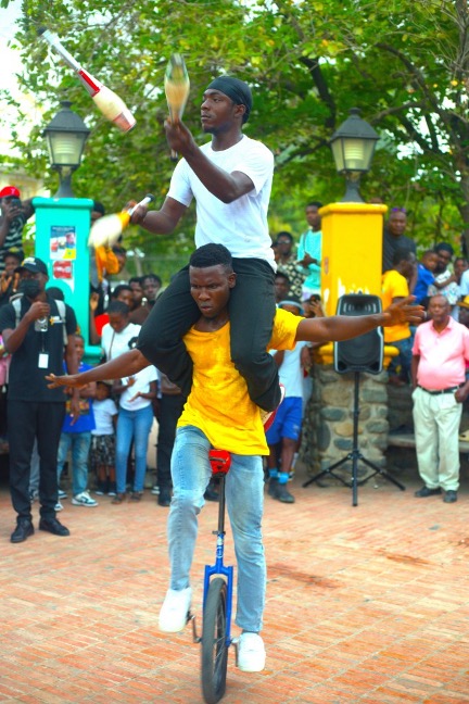 Ericson ‘Smoky G’ Germéus juggles while sitting on Davideson Desamours’s shoulders who is riding a unicycle. Photo by Onz Chéry/ The Haitian Times