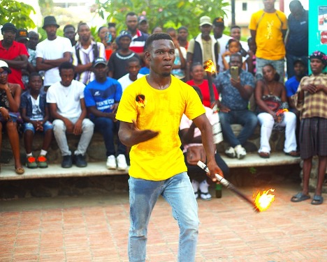 Davideson Desamours juggles three lit torches. Attendees watch him in awe. One man holds his phone up to record Desamours. Photo by Onz Chéry/ The Haitian Times