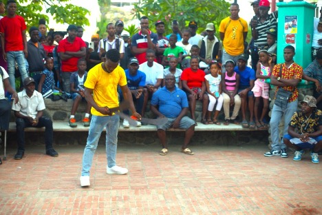 Davideson Desamours looks down as he holds three machetes. Attendees watch him in awe, some smile while others hold their phones up to record him. Photo by Onz Chéry/ The Haitian Times 